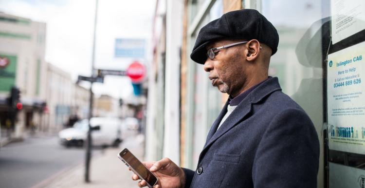 Man wearing a suit leaning on the side of a building and looking at his phone