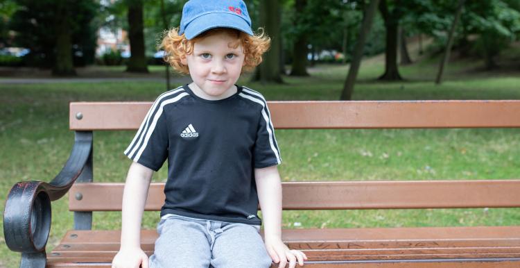 Young boy sitting on a park bench wearing a blue cap