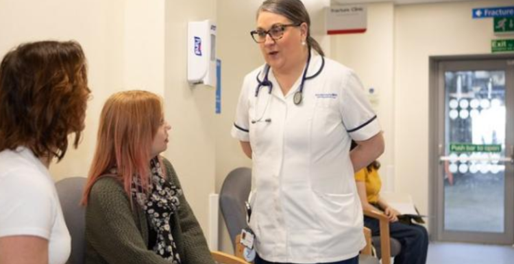 A nurse talking to two female patients in the hospital corridor as they wait for their appointment
