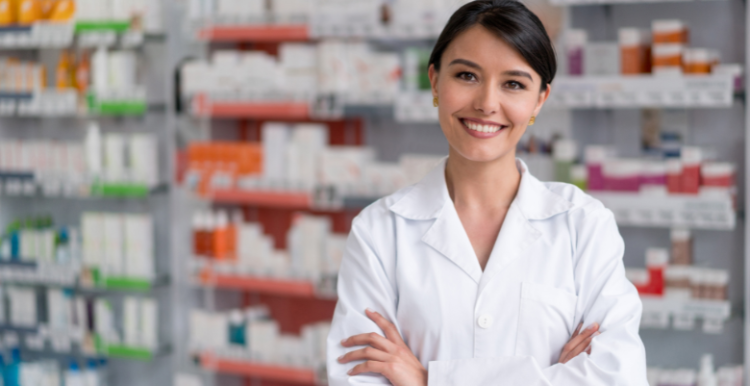 A pharmacist smiling and the background is shelves of medications.