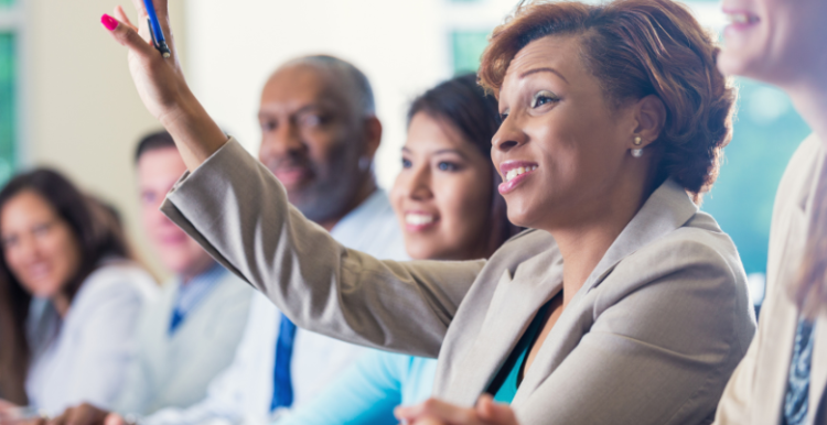 a group of people attending a conference and a woman raising her hand to ask a question.