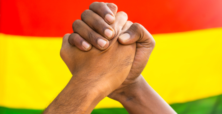 Two diverse hands joining hands against black history month flag to show unity.