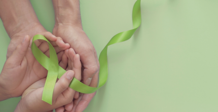 Two hands holding a light green ribbon for world mental health day.