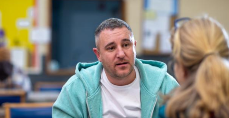 Man in white shirt and blue hoodie talking to a lady.