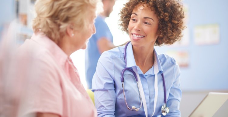 NHS doctor sitting next to a female patient and talking to them during their appointment.