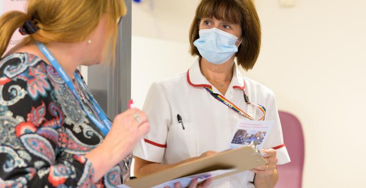 A nurse wearing a face mask who is talking to a healthcare professional..