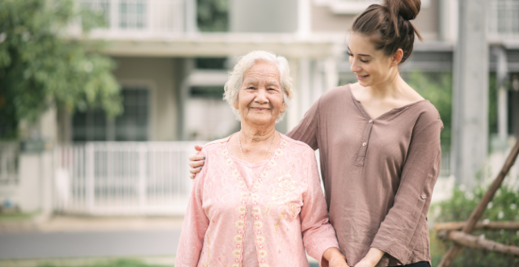 A young female putting holding an elderly woman and smiling to support her.