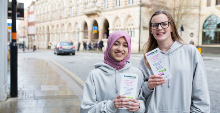 Two young healthwatch volunteers standing together outside and holding leaflets.
