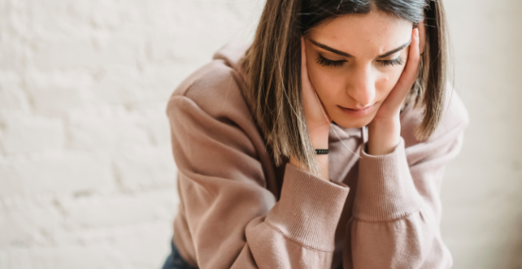 A sad woman sitting down with her hands on her cheeks.