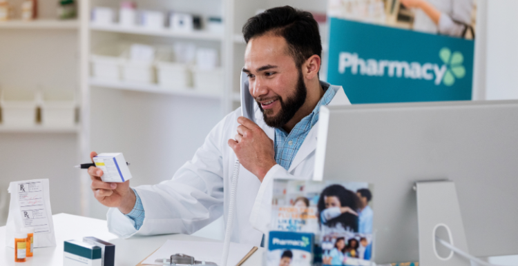A male pharmacist on the phone whilst holding a medicine in his hands.