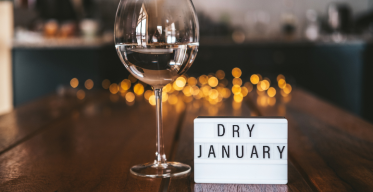 A wooden table with a cup of wine and a sign that says "dry January"