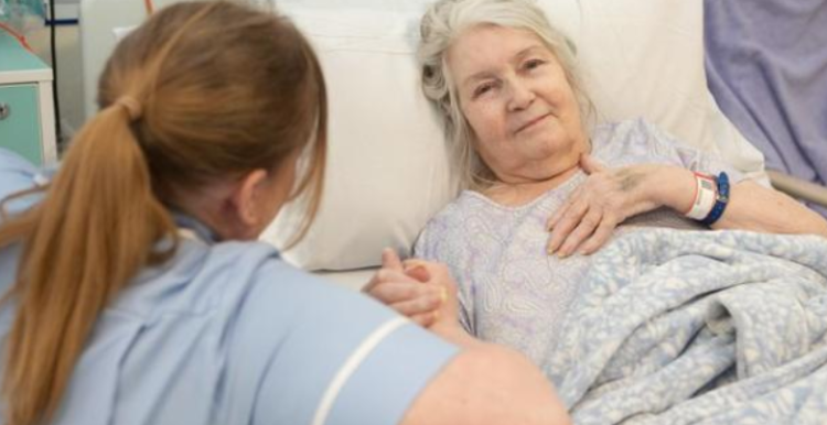 A woman lying in bed at the hospital holding a female nurse's hands.