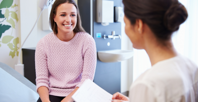 A young female patient sitting down and smiling during her appointment with a female doctor.