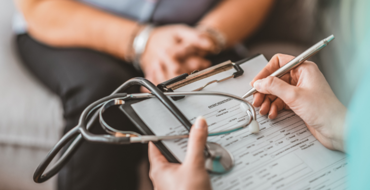 A healthcare professional writing information on a paper attached to a clip board.