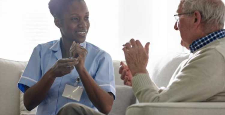 A female medical professional communicating with an elderly man through sign language.
