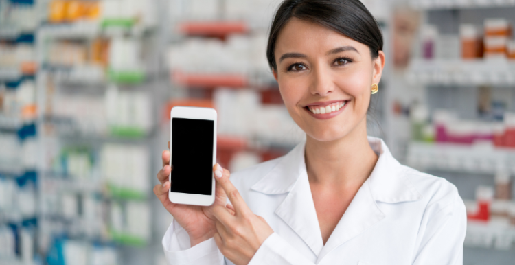 A female pharmacist smiling in a pharmacy and holding up a smartphone