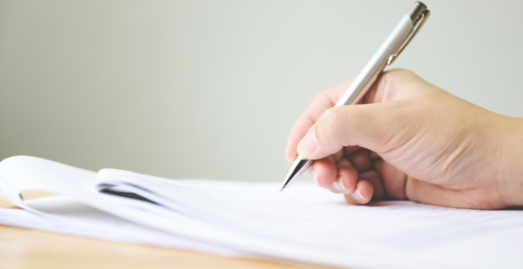 A hand holding a pen and signing documents