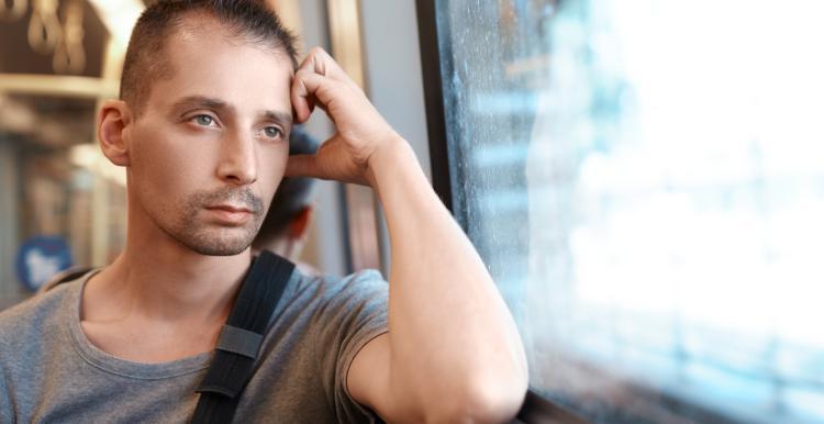 A man looking outside the window with hand on his head