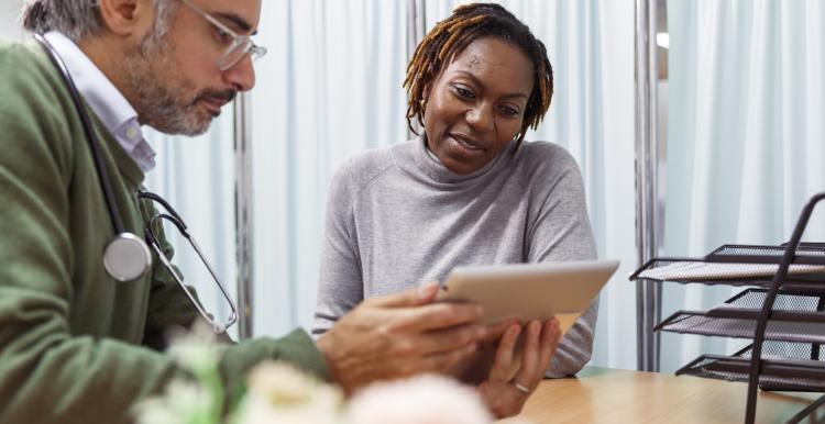 A male doctor holding a tablet device and talking to a female patient