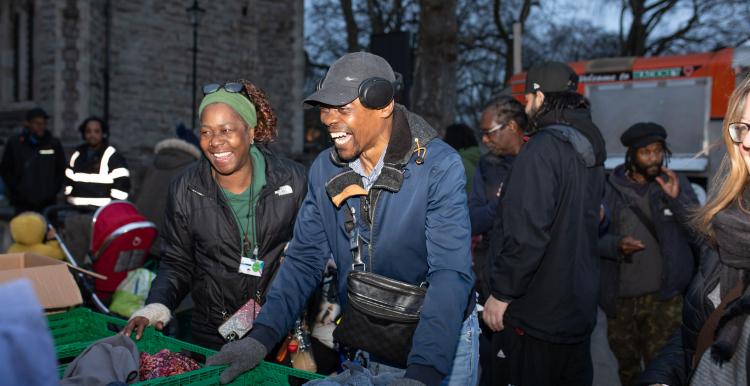 A black man and woman standing by two crates of donations as they volunteer