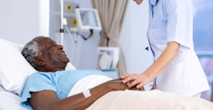 A male patient lying down on a hospital bed and smiling at a female nurse as she puts her hands on his to comfort him