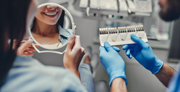 Woman at a dental clinic smiling in the mirror and the male dentist is sitting next to her holding the dental equipment