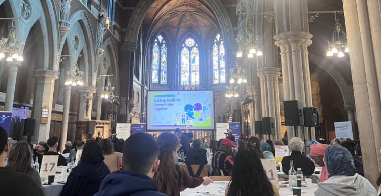 Attendees sitting in a hall looking at a screen during the community champions event