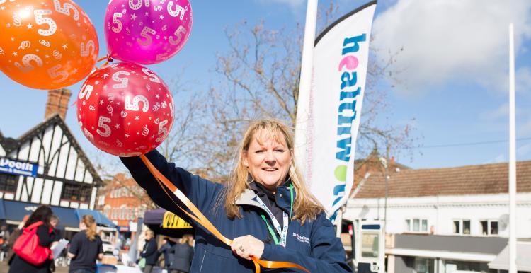 Healthwatch staff member holding balloons at a community event
