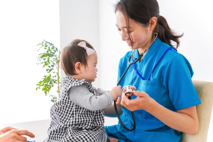 A female nurse holding a baby's hands as they both smile.