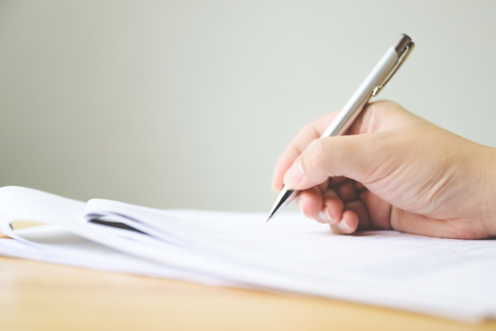 A hand holding a pen and signing documents