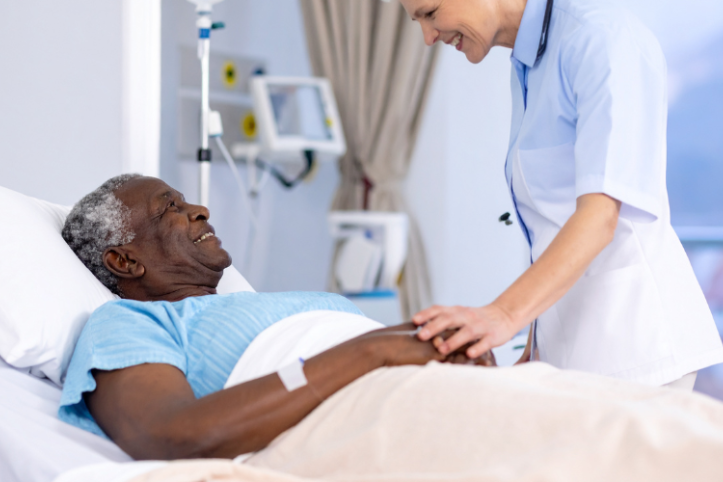 A male patient lying down on a hospital bed and smiling at a female nurse as she puts her hands on his to comfort him
