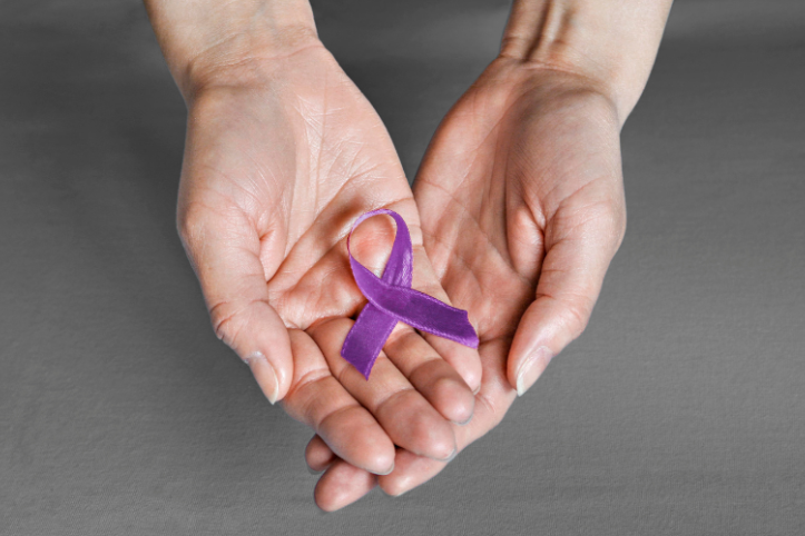 Two hands holding a purple ribbon to represent pancreatic cancer