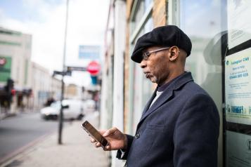 Man wearing a suit leaning on the side of a building and looking at his phone