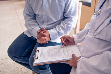 a doctor and a patient filling in a document, their heads not visible in the photo