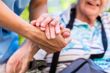 A picture of a nurse holding an elderly patients' hand.