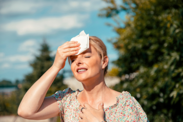 Picture of a lady standing in the sun holding a tissue to her head to prevent sweating.