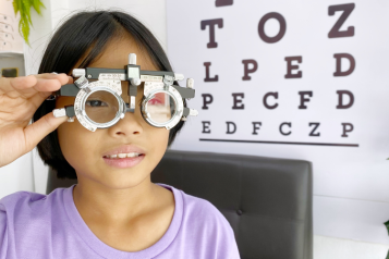 Picture of a child holding eyecare testing equipment against their eyes.