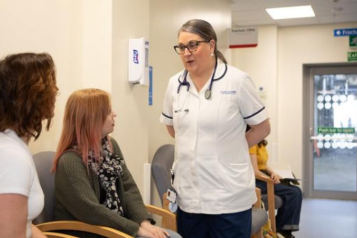 A nurse talking to two female patients in the hospital corridor as they wait for their appointment