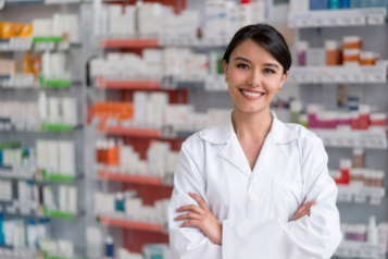 A pharmacist smiling and the background is shelves of medications.