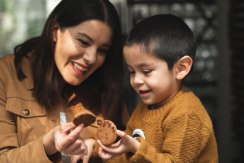 A mother and child holding biscuits together and smiling.