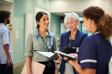 A doctor, nurse and hospital manager holding a report and discussing with eachother in a hospital hallway.