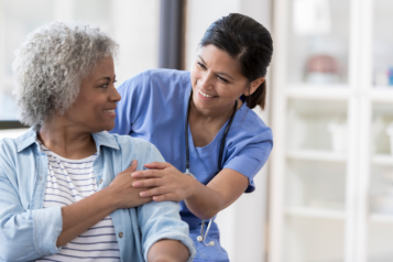 A doctor putting hand on the shoulder of a patient as they smile at eachother.