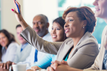 a group of people attending a conference and a woman raising her hand to ask a question.