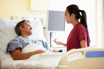 A doctor talking to a patient in a hospital bed as they both smile at eachother.