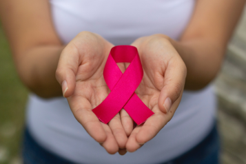Two hands holding a pink ribbon for breast cancer awareness.