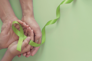 Two hands holding a light green ribbon for world mental health day.