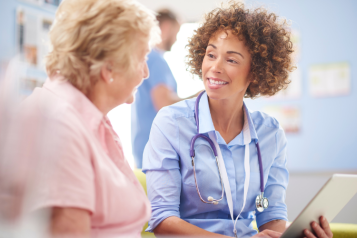 NHS doctor sitting next to a female patient and talking to them during their appointment.