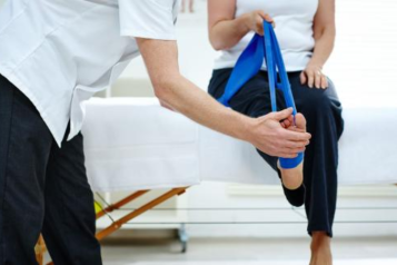 A doctor supporting a patient to do resistance training exercises to strengthen their leg.