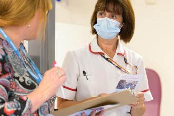 A nurse wearing a face mask who is talking to a healthcare professional..