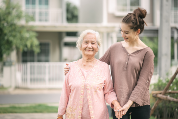 A young female putting holding an elderly woman and smiling to support her.